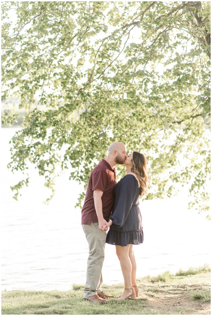 engaged couple kissing and holding hands under tree at marsh creek state park