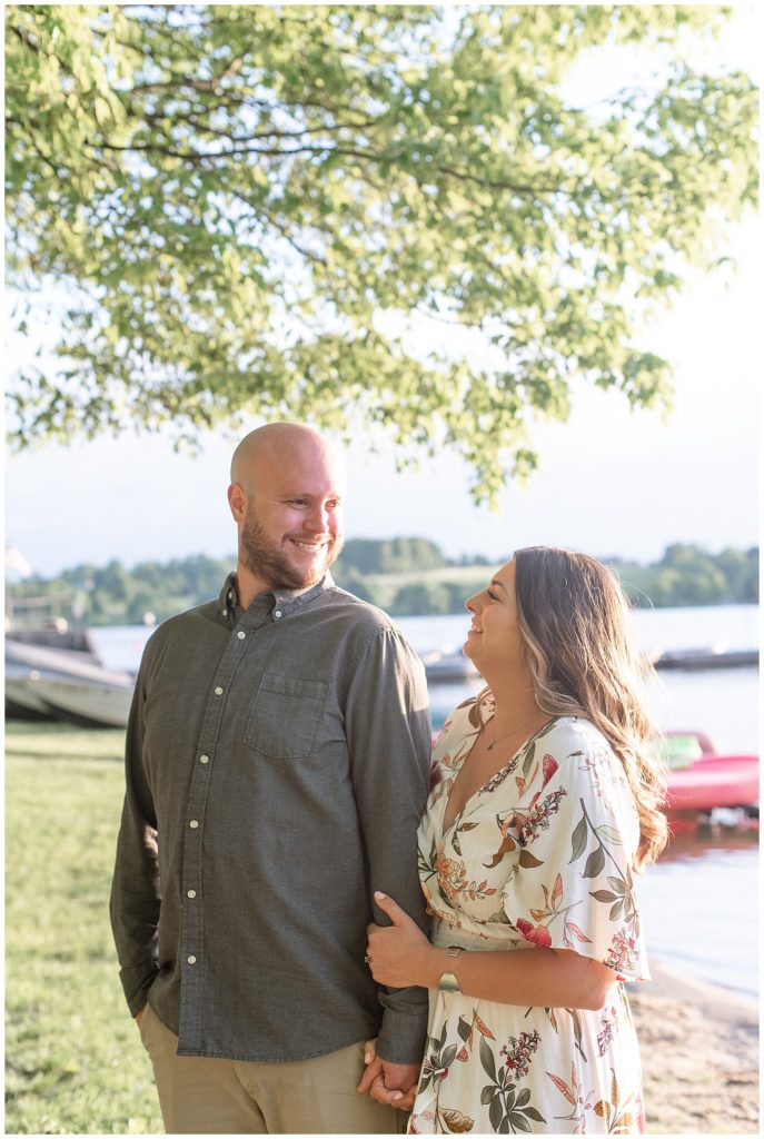 engaged couple smiling at each other as woman hold's onto man's left arm by water at marsh creek state park in chester county