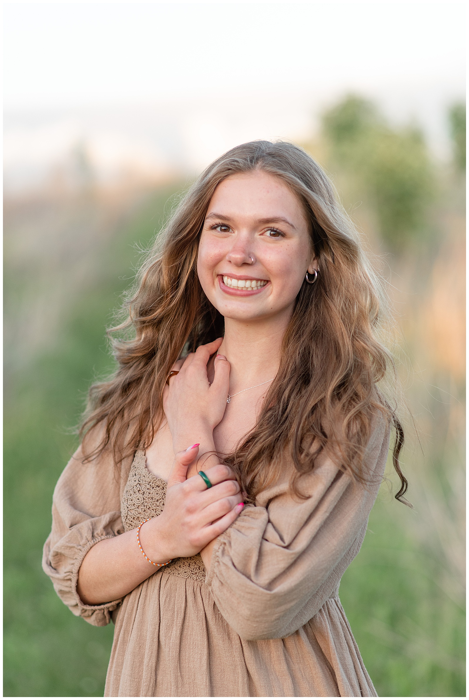 senior girl smiling at camera with her hands folded over her chest at sunset in lancaster county