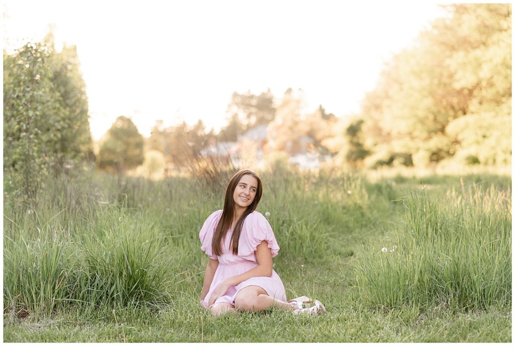 senior girl sitting in tall grasses at overlook park looking towards the sky in light pink dress in manheim township