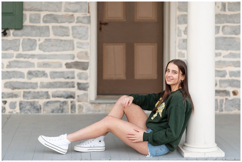 senior girl leaning against white column on front porch wearing baylor university sweatshirt at overlook park