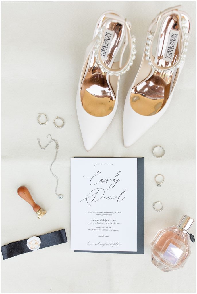 wedding invitation with wedding rings, bride's white shoes, and a bottle of perfume in lancaster county