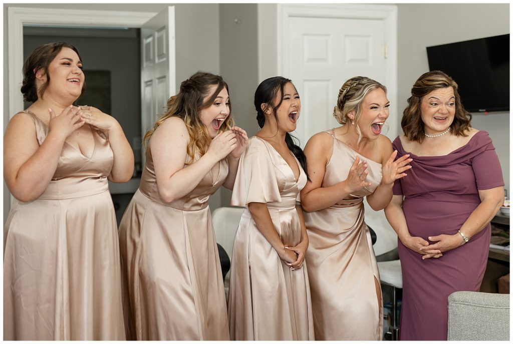 four bridesmaids and bride's mom all reacting with excitement at seeing the bride for the first time in bridal suite at cameron estate inn