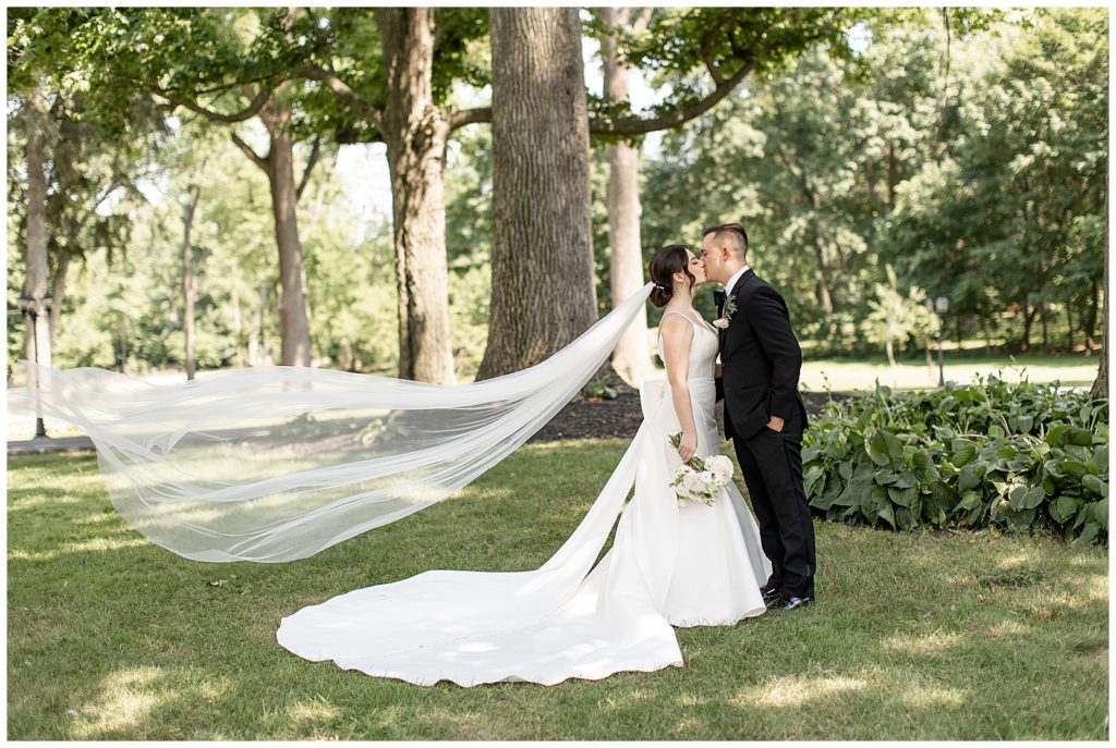 bride and groom kissing on lawn with bride's dress train displayed and veil blowing in breeze at cameron estate inn