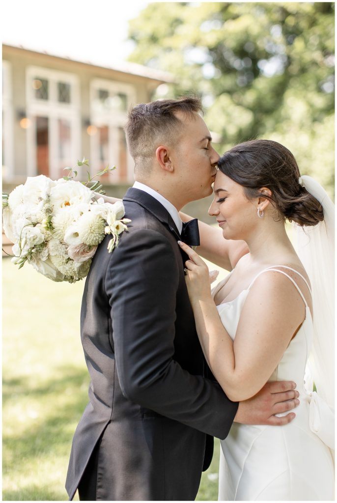 couple hugging as groom kisses bride's forehead with their eyes closed at cameron estate inn