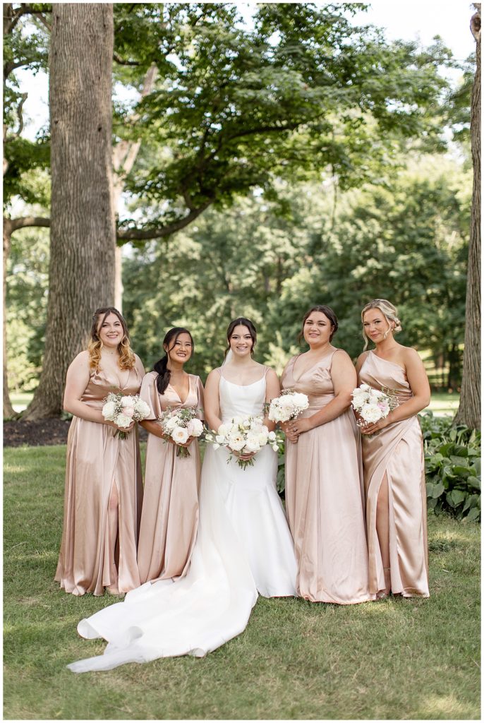 bride surrounded by her four bridesmaids wearing blush gowns and holding bouquets outside at cameron estate inn