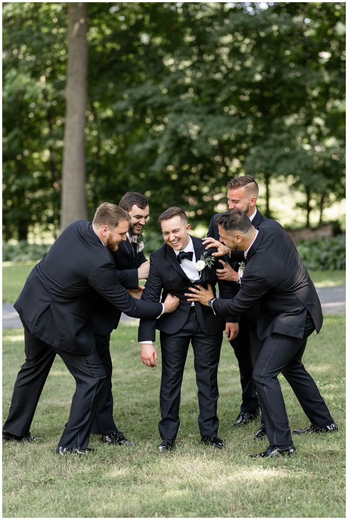 groomsmen being playful and having fun with groom on lawn of cameron estate inn in mount joy pennsylvania