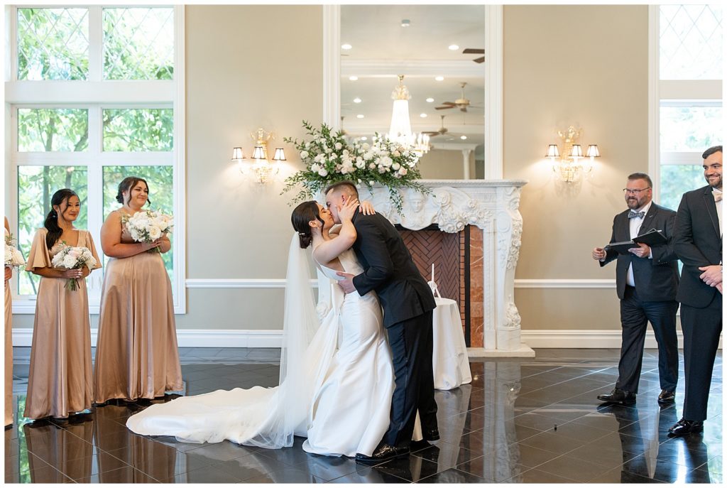 couple sharing their first kiss during wedding ceremony by fireplace at cameron estate inn