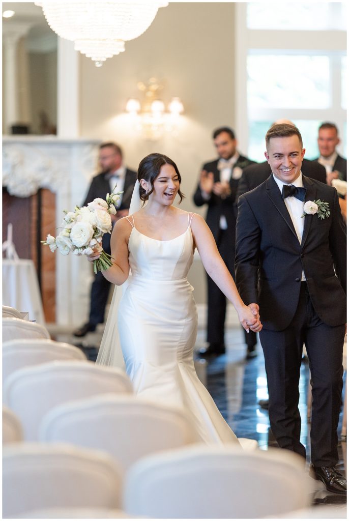 couple holding hands and smiling as they walk back aisle after wedding ceremony at cameron estate inn