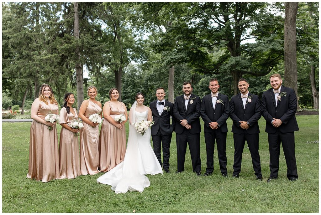 bride and groom with their bridal party all standing on lawn and smiling at cameron estate inn