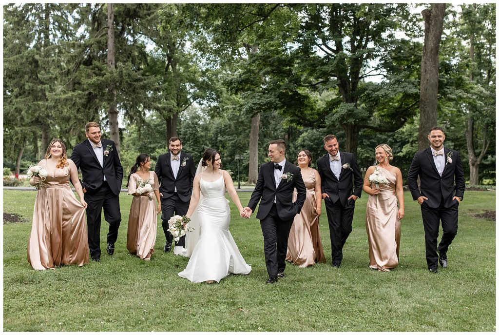 bride and groom holding hands and looking at each other and walking with bridal party toward camera in lancaster county