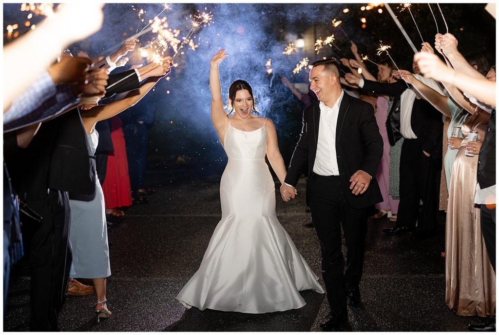 bride and groom leaving reception at nighttime during sparkler sendoff as bride raises her right hand in lancaster county pennsylvania