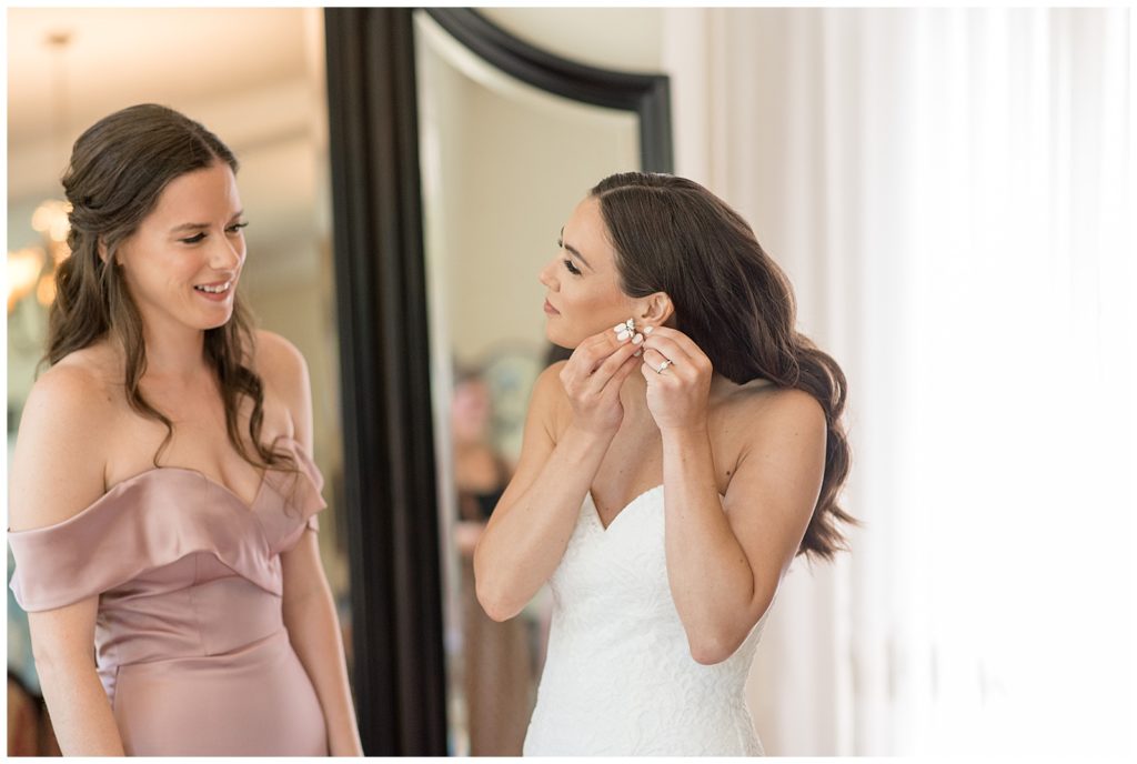bride putting on her left earring with her bridesmaid in bridal suite at parque ridley creek