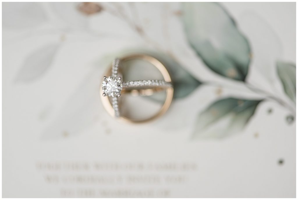 diamond wedding ring resting inside groom's gold wedding band atop wedding invitation