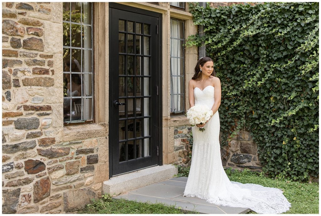 bride in strapless white gown holding beautiful white bouquet and looking over left shoulder outside building with black door in pennsylvania