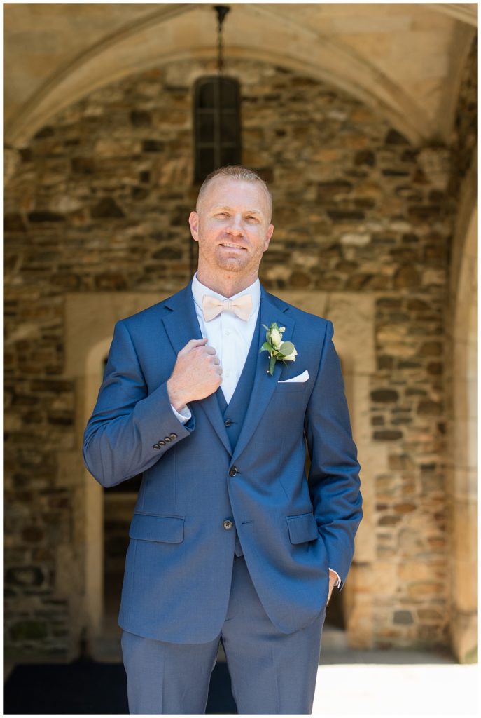 groom holding edge of his navy blue suit coat with right hand as he smiles at parque ridley creek