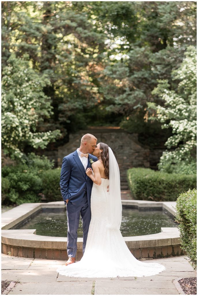 bride and groom kissing by outdoor fountain and landscaped garden at parque ridley creek