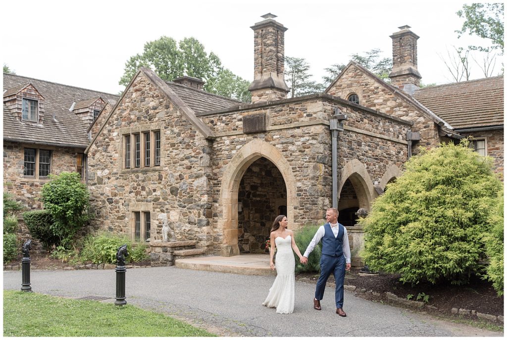 bride and groom holding hands as they walk in front of historic building at parque ridley creek in pennsylvania