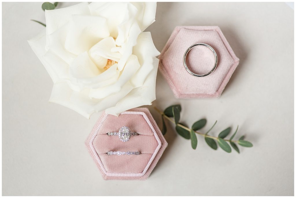 silver wedding rings resting inside light pink velvet ring box by white rose at elizabeth furnace