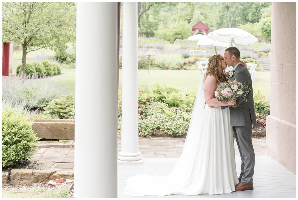 bride and groom kissing on front porch by white columns on summer day at elizabeth furnace