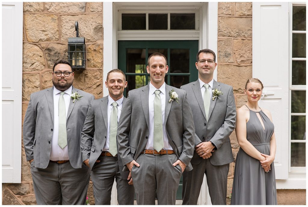 groom surrounded by his groomsmen all wearing gray suits and ties by stone building at elizabeth furnace
