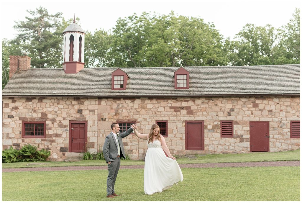 groom twirling his bride outside in lawn by old stone building with maroon doors and windows in lititz pa 