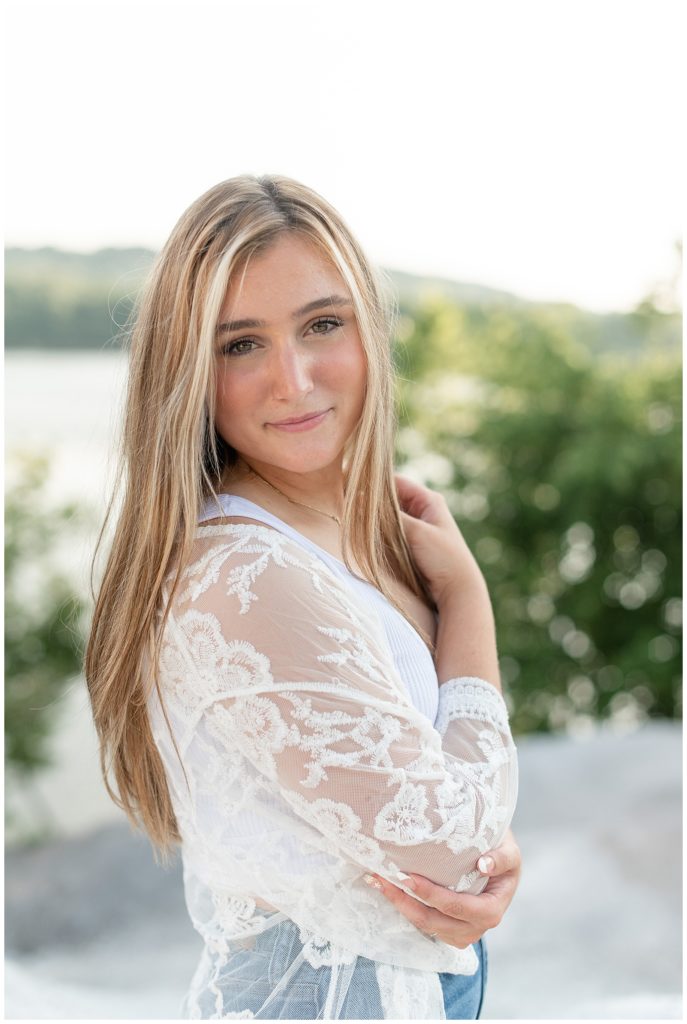 senior girl in white lacy shirt with right shoulder toward camera on sunny evening in lancaster, pennsylvania