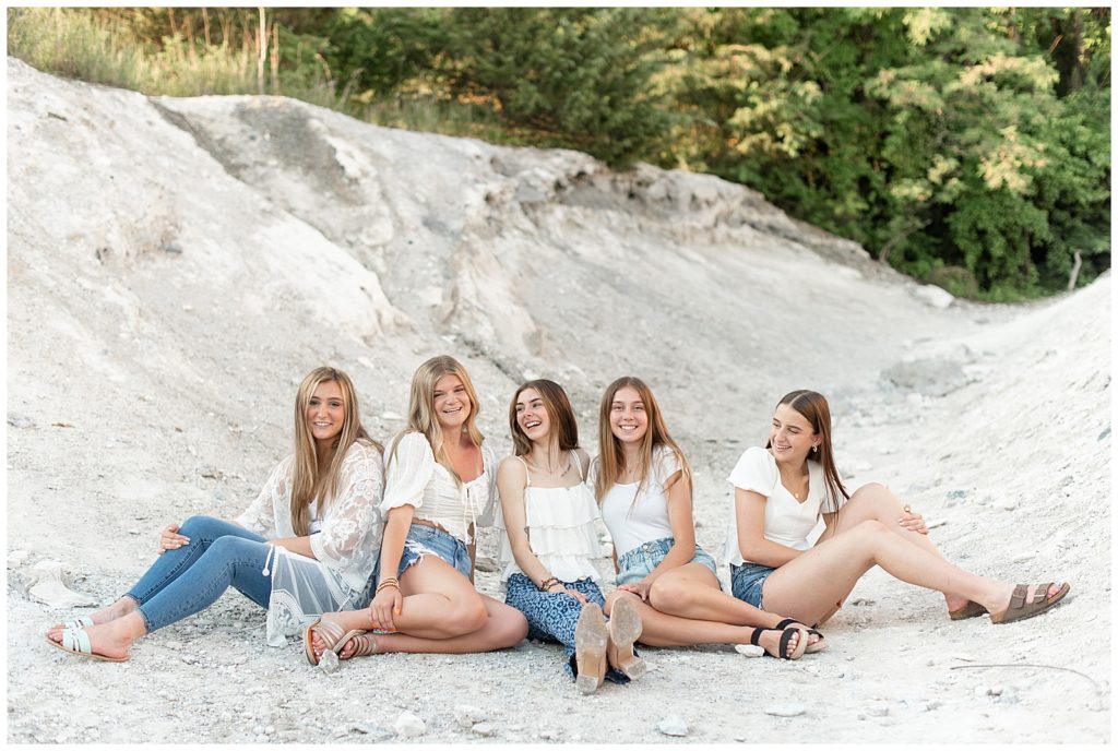 five senior girls sitting on large white rock and smiling and looking at each other at the white cliffs of conoy