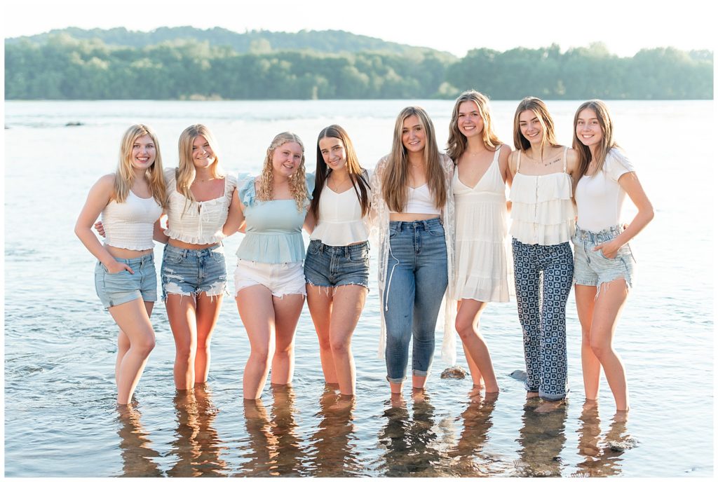 senior girls side by side with their arms around each other's back standing in shallow water of susquehanna river in lancaster pennsylvania