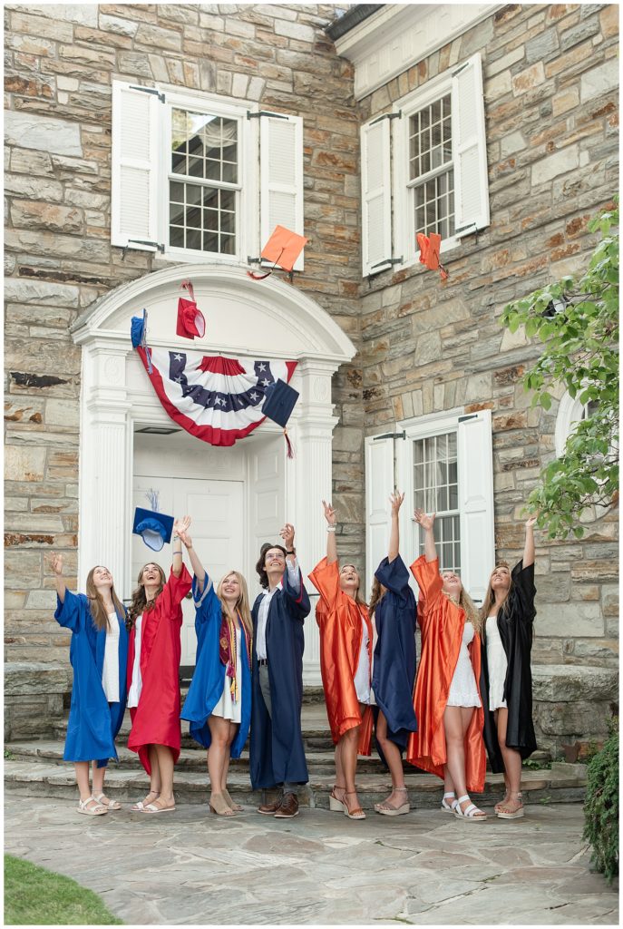 eight senior spokesmodels in colorful graduation gowns throwing their caps into the air in downtown lititz in lancaster county