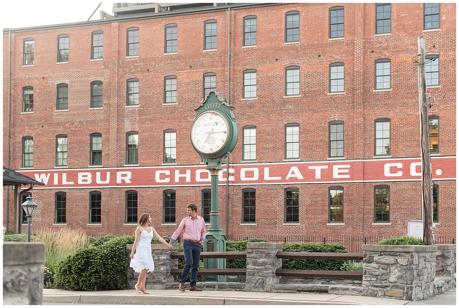 engaged couple holding hands as guy leads girl along sidewalk by old wilbur chocolate company factory