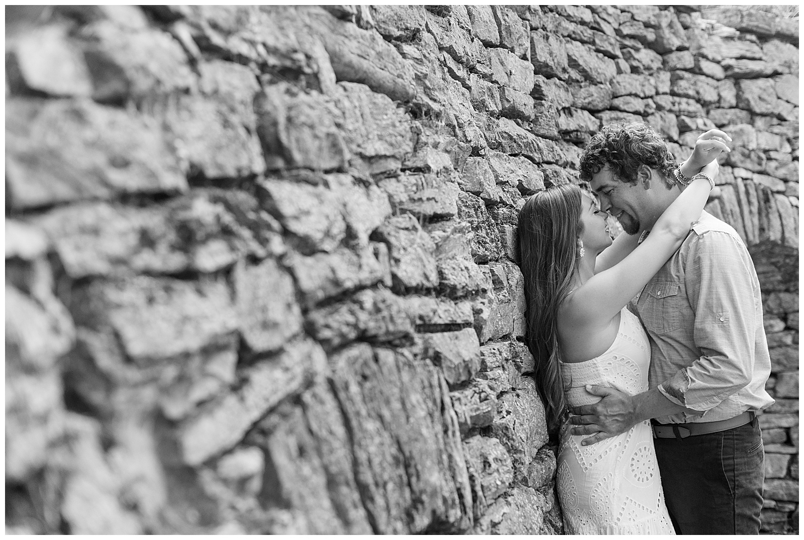 black and white photo of engaged couple almost kissing as girl leans back against stone wall in lititz pennsylvania