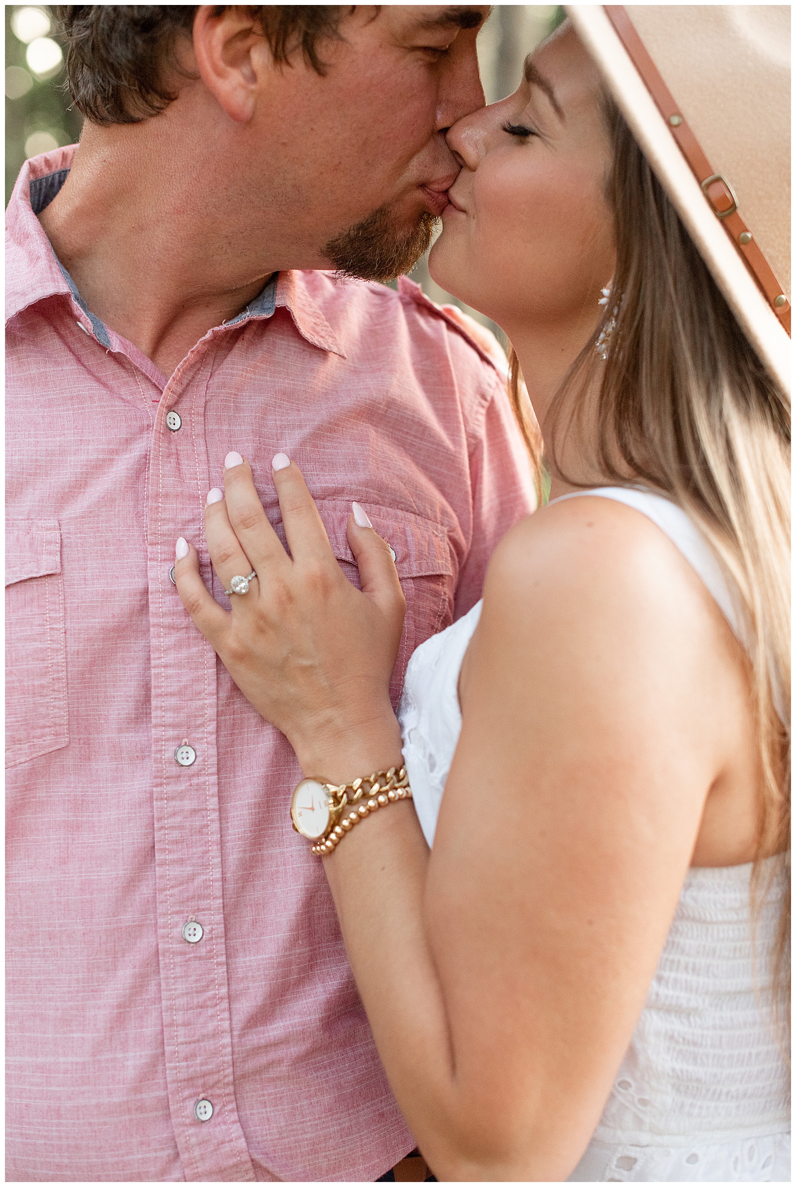 guy wearing light pink button-up shirt kissing girl in white dress as she shows her engagement ring on his chest in lancaster county