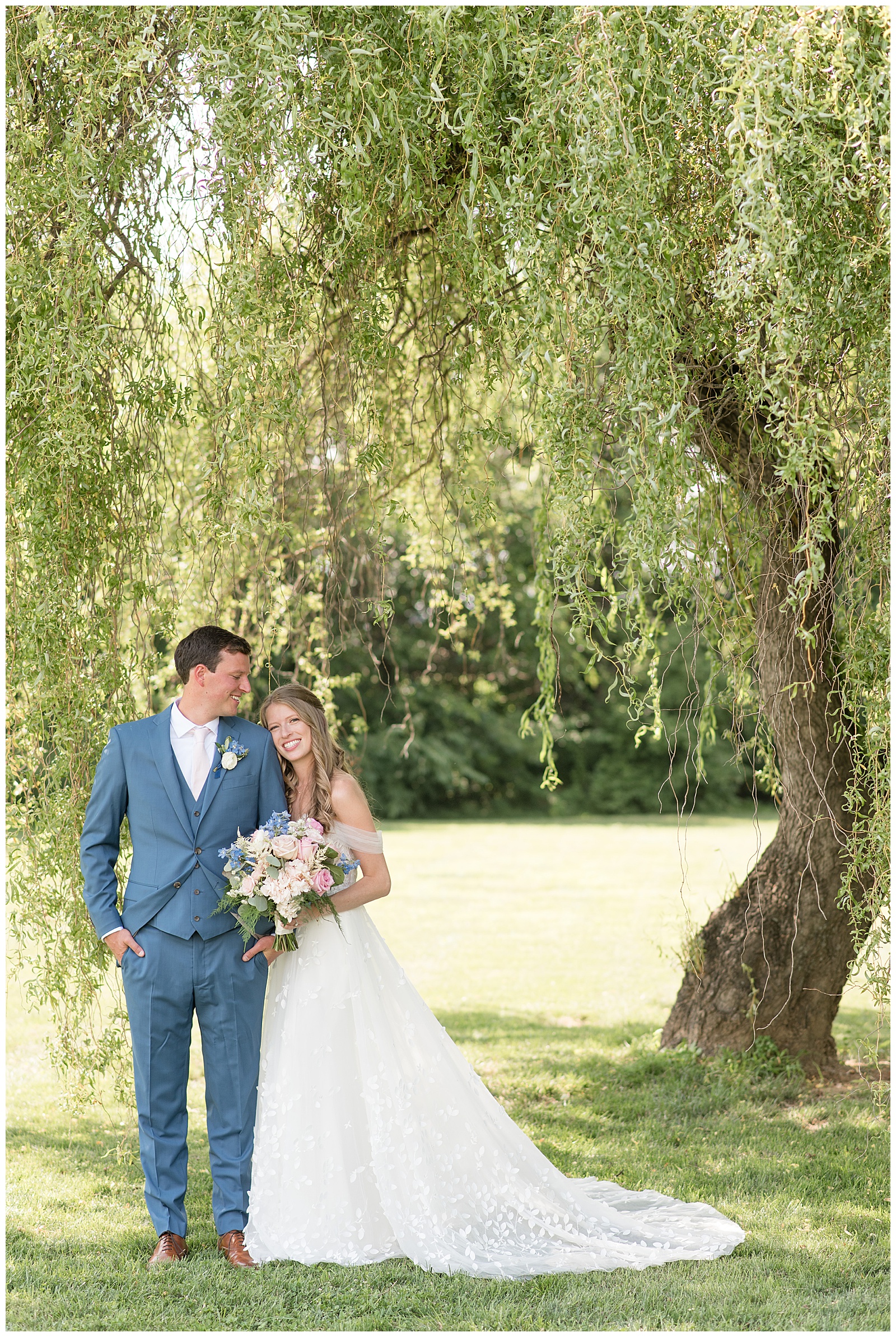 bride resting her right cheek against groom's left shoulder as she looks down at her under willow tree in lancaster pennsylvania