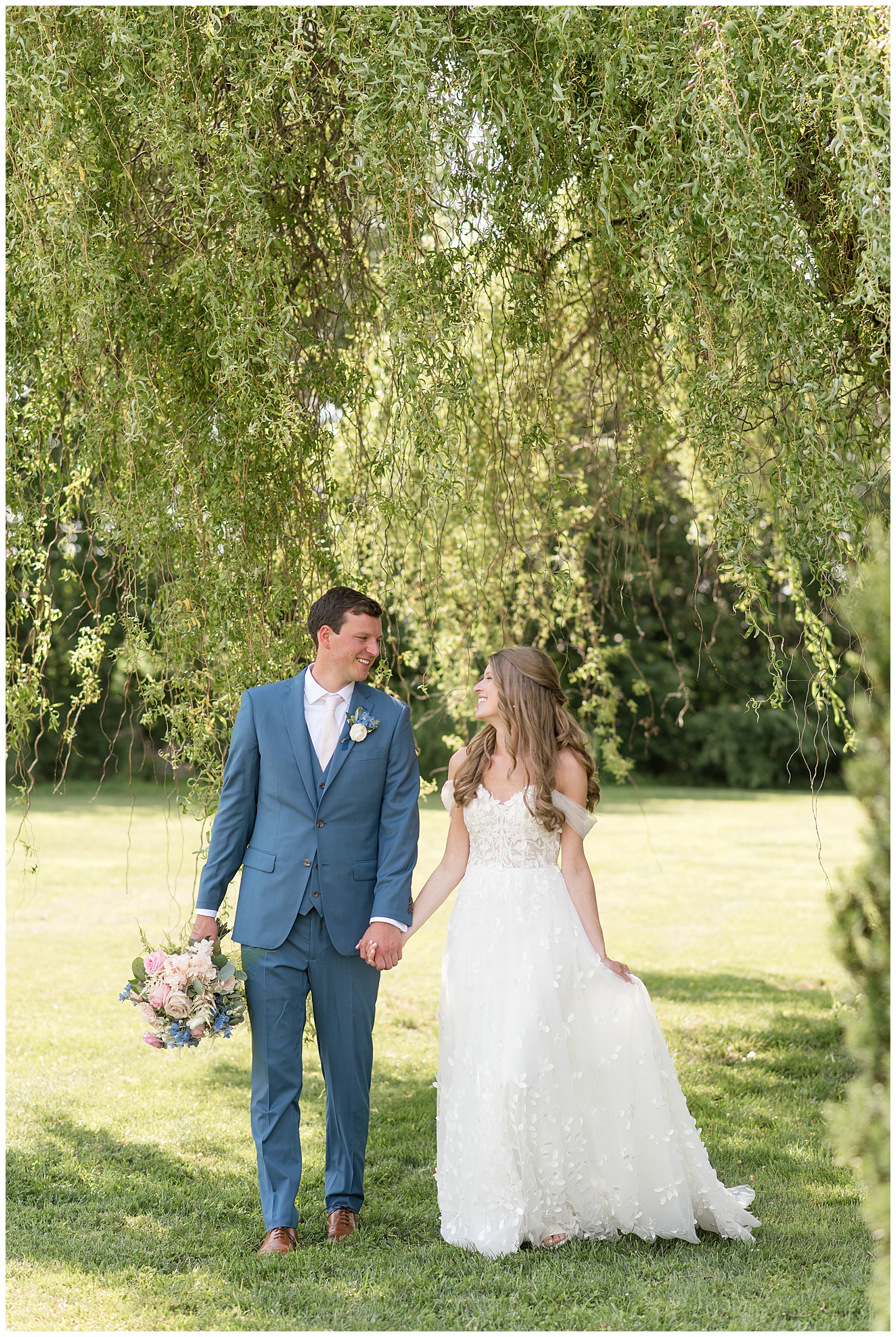 bride and groom holding hands as they look at each other walking towards camera under willow tree in lancaster county