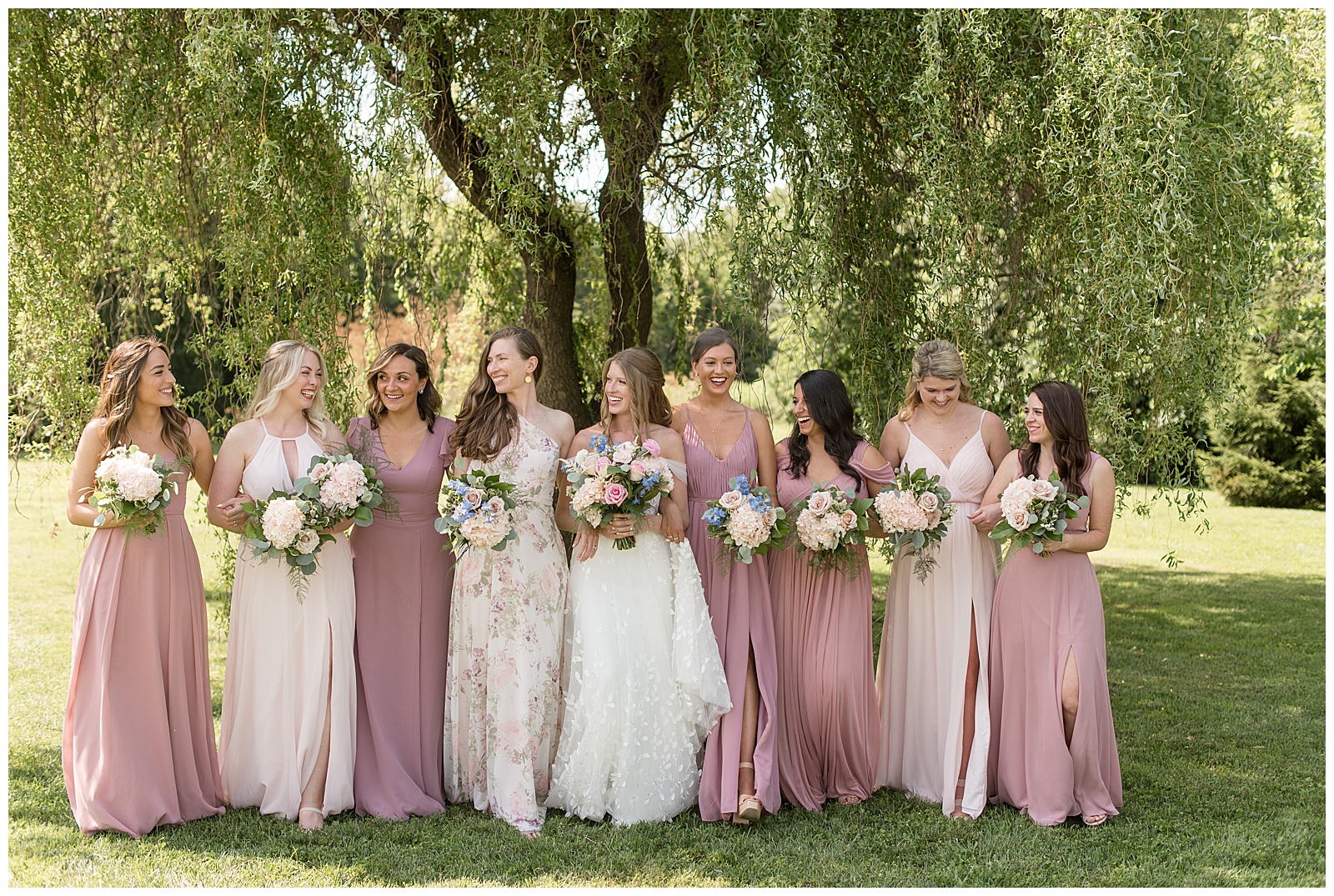 bride with her bridesmaids in blush gowns all holding bouquets and walking towards camera at the barn at silverstone
