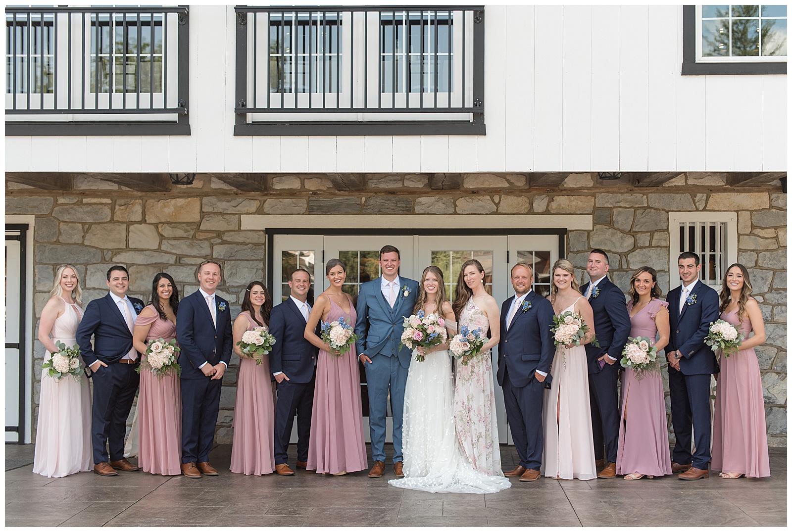 couple surrounded by their bridal party outside white barn on sunny day at the barn at silverstone