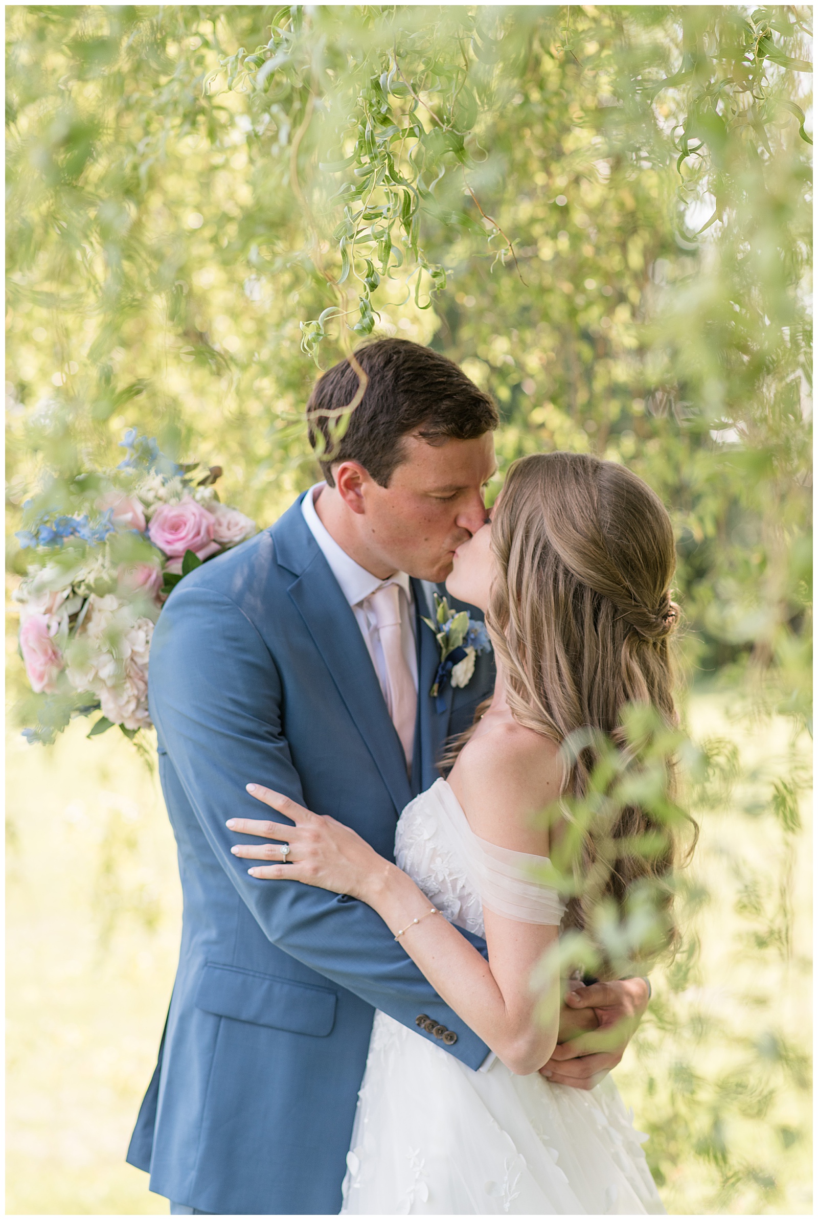 bride in off-the-shoulder gown kissing her groom in flue suit with pink tie at the barn at silverstone