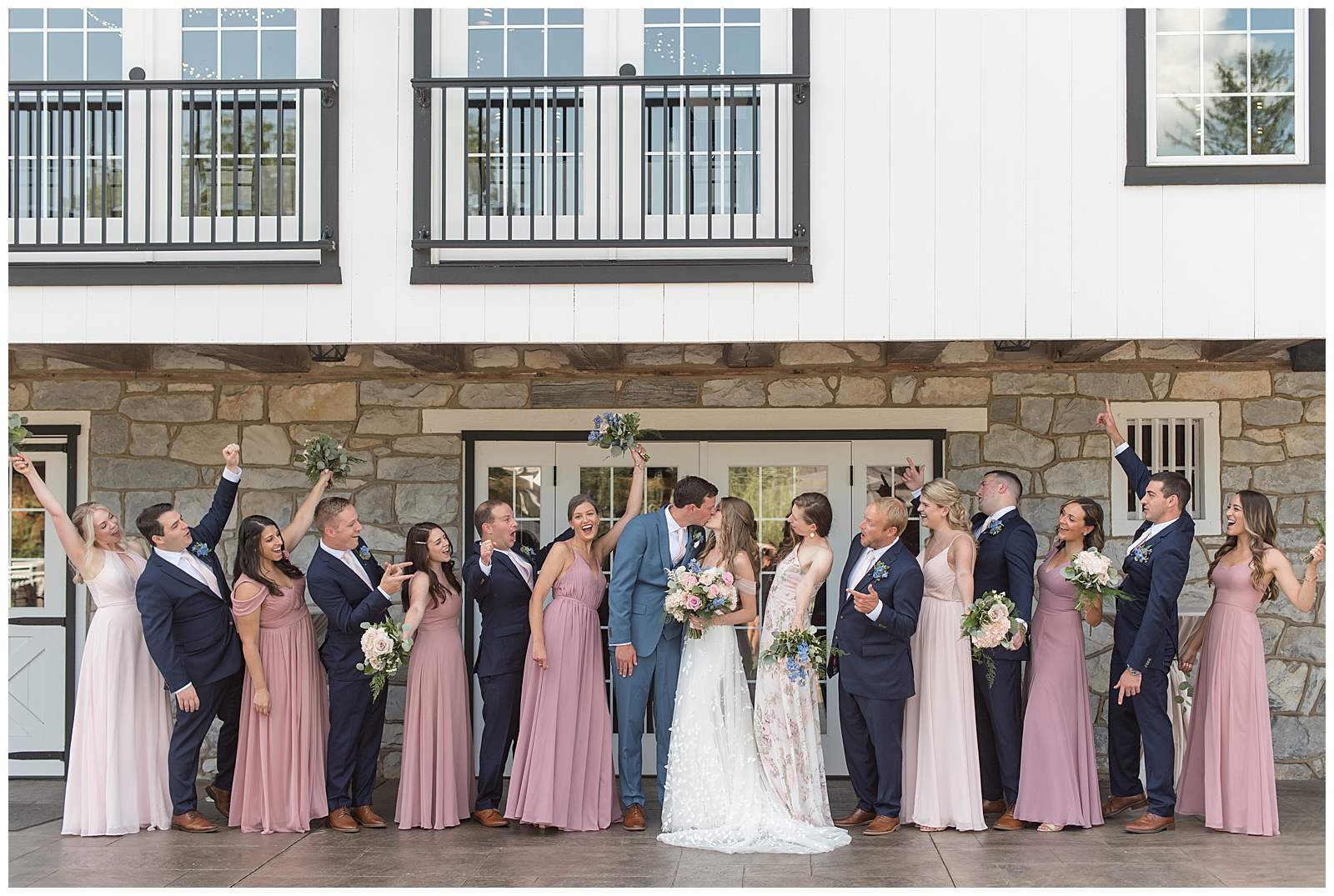 couple kissing as their bridal party cheers for them by historic barn in lancaster county pennsylvania