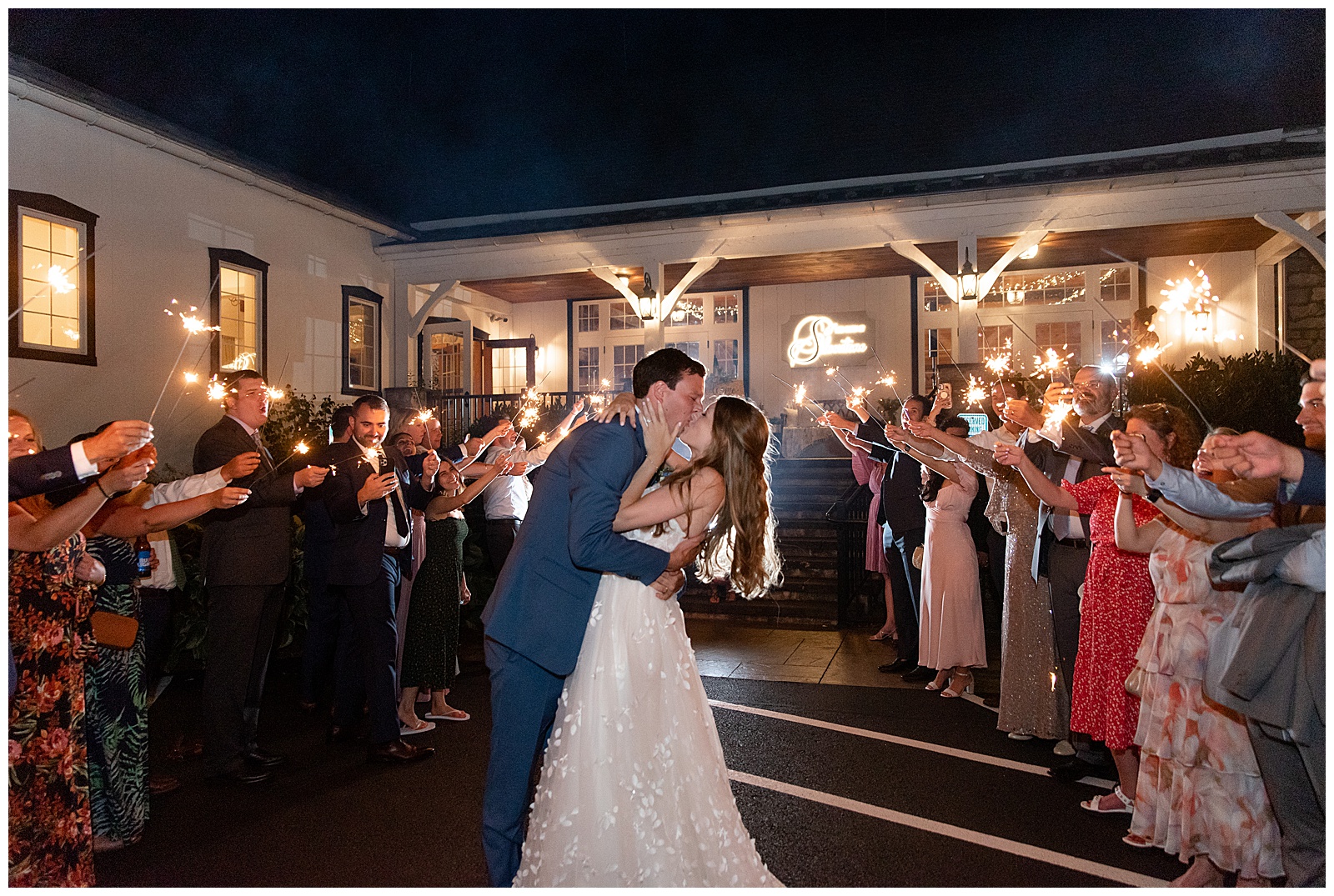 couple sharing a kissing in aisle of guests holding sparklers as they leave at nighttime from their reception at the barn at silverstone