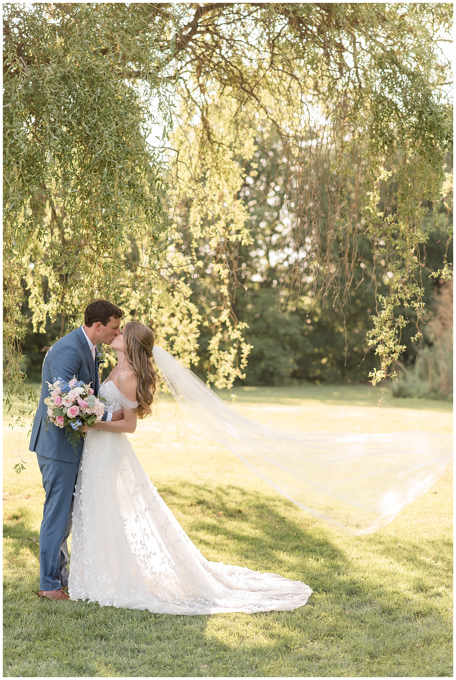bride and groom kissing under willow tree on sunny summer day at the barn at silverstone
