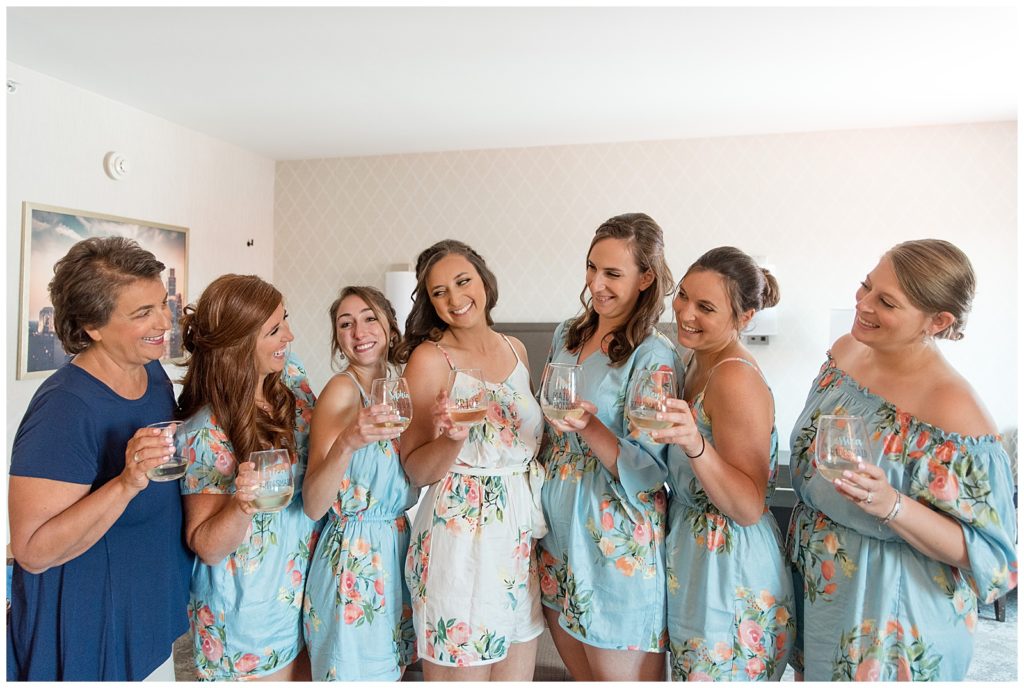 bride surrounded by her mom and five bridesmaids all wearing floral dresses inside bridal suite at normandy farms