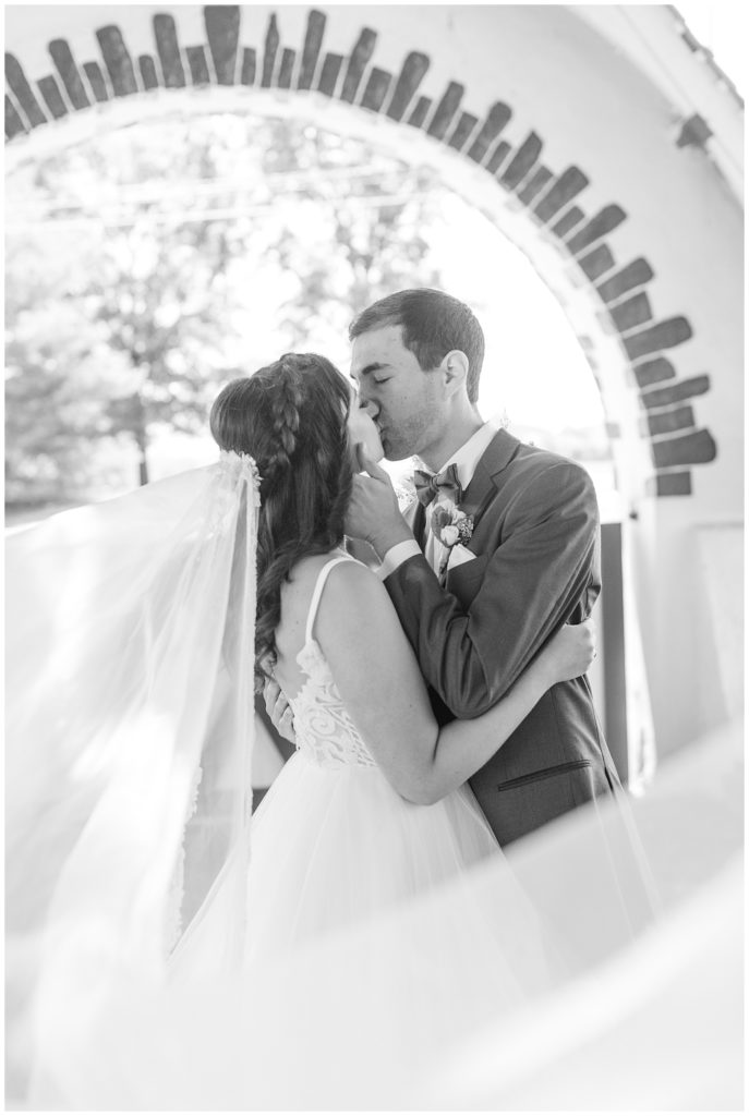 black and white photo of couple kissing with her long white veil blowing around them at normany farms in blue bell pennsylvania