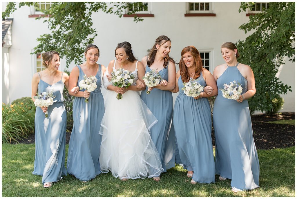 bride and her bridesmaids all holding bouquets and walking towards camera while smiling and look at each other at normandy farms