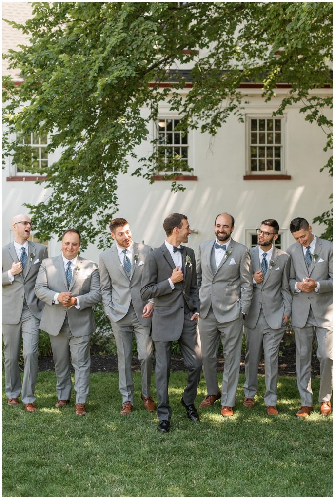 groom looking back at his five groomsmen all wearing gray suits and smiling at normandy farms