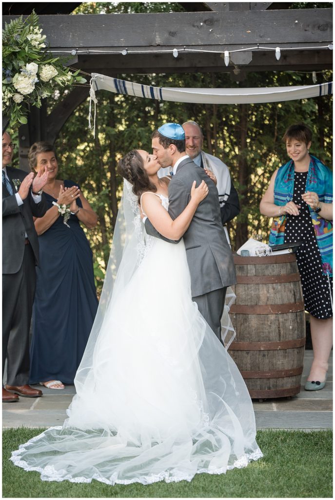 bride and groom kissing during traditional jewish wedding with guests clapping at normandy farms