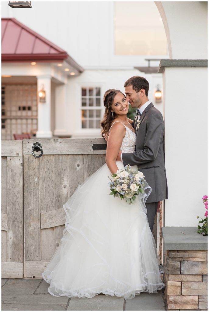bride smiling with right shoulder toward camera and holding bouquet as groom kisses her left cheek at normandy farms