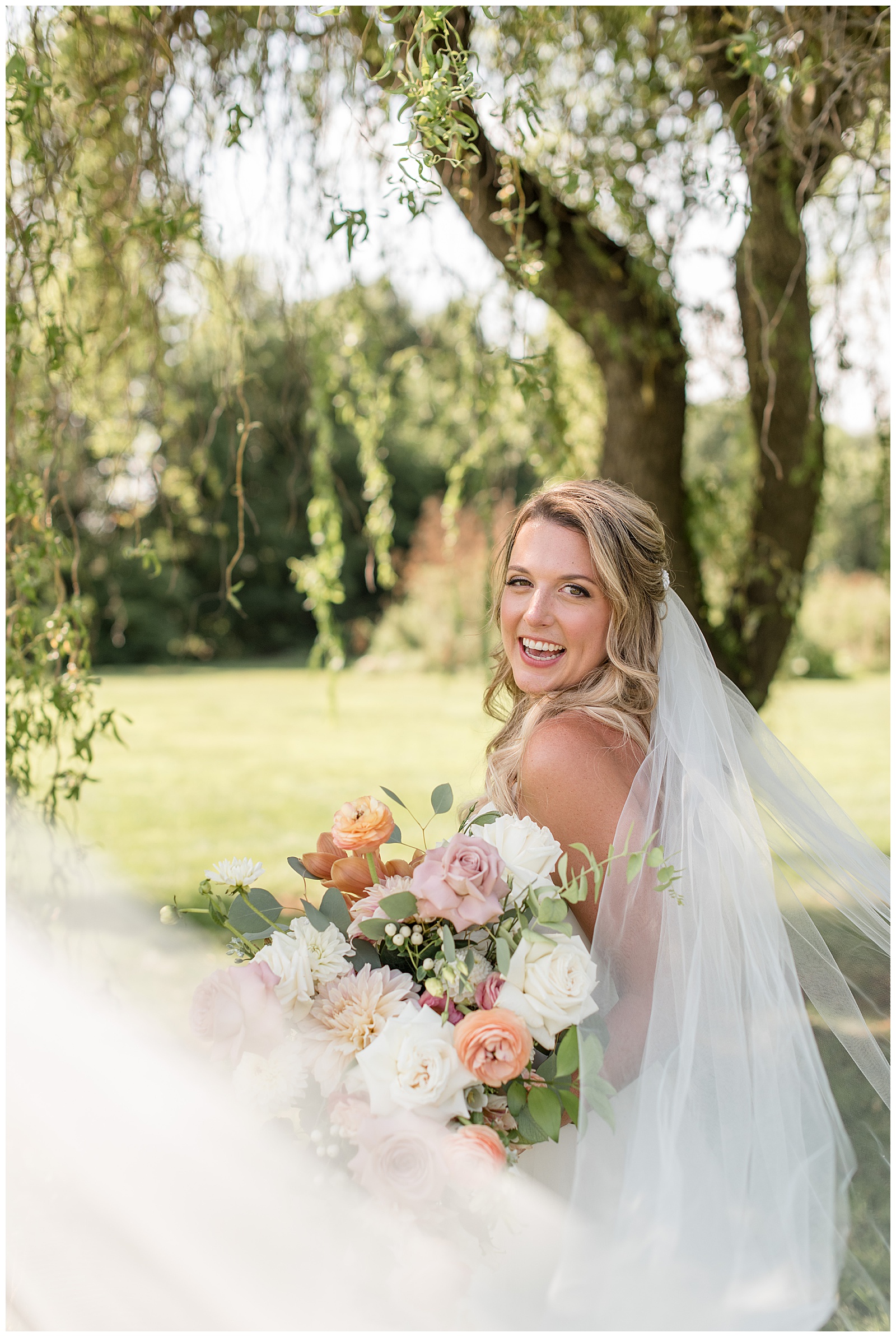 bride smiling with long veil blowing by camera as she holds pink and white bouquet in lancaster pennsylvania