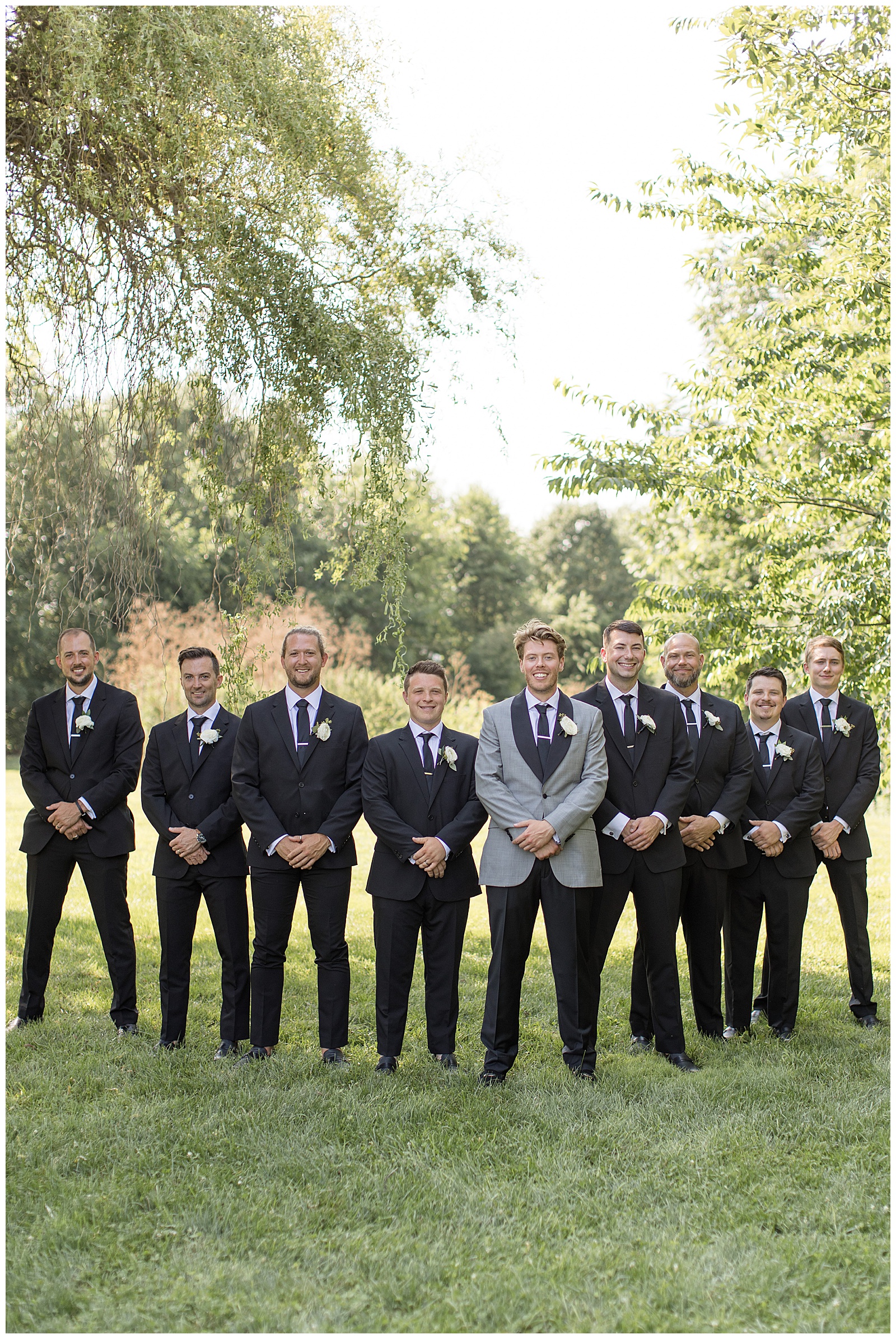 groom with his eight groomsmen all with hands folded in front of them at the barn at silverstone