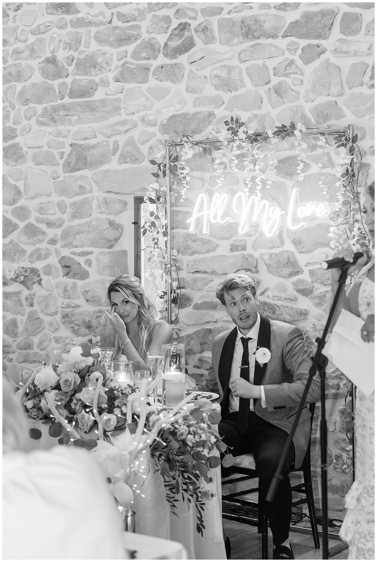 black and white photo of couple during barn reception as guest speaks at the barn at silverstone